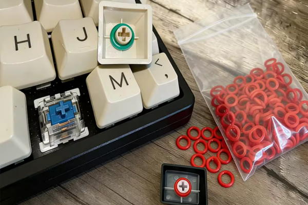 Teclado com keycaps removidos expondo um switch, ao lado de saquinho de o-rings vermelhos